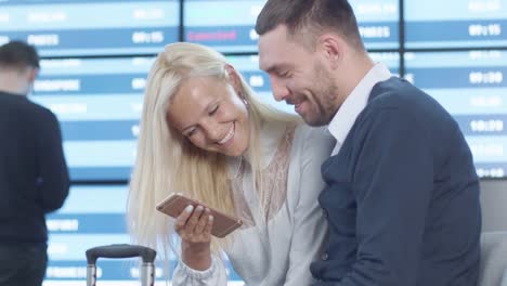 Man-and-Woman-using-Phone-Together-while-Waiting-Boarding-at-Departure-Lounge-at-the-Airport.