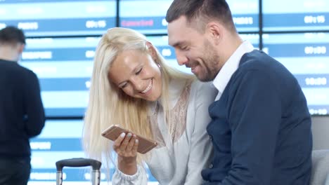 Hombre-y-mujer-usando-el-teléfono-juntos-mientras-espera-embarque-en-el-salón-de-salidas-en-el-aeropuerto.