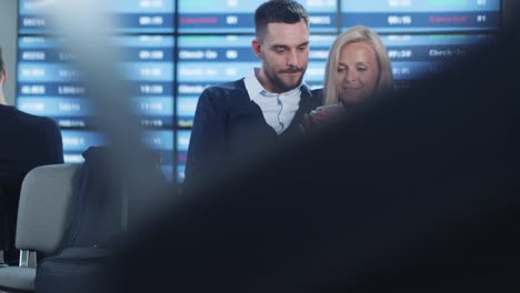 Hombre-y-mujer-usando-el-teléfono-juntos-mientras-espera-embarque-en-el-salón-de-salidas-en-el-aeropuerto.