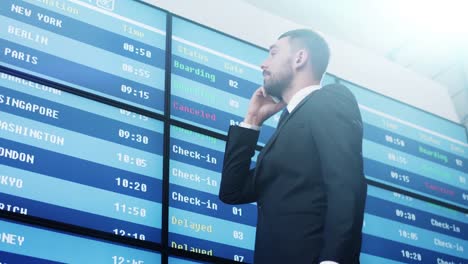 Businessman-talking-on-Mobile-Phone-while-Looking-at-Information-Board-at-the-Airport.