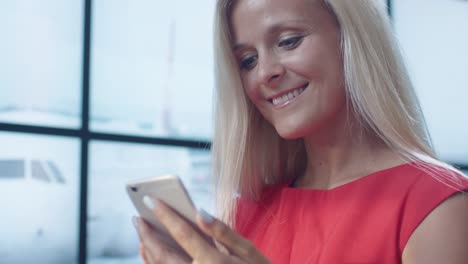 Attraktive-Blonde-lächelnde-Frau-mit-Handy-in-der-Abfluglounge-am-Flughafen.