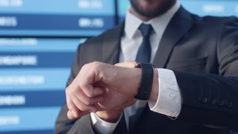 Businessman-Looking-Smart-Watch-while-Standing-next-to-Information-Board-in-the-Airport.