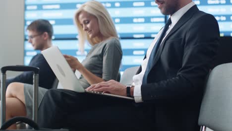 Hombre-de-negocios-trabajando-en-ordenador-portátil-mientras-espera-el-embarque-en-la-sala-de-embarque-en-el-aeropuerto.