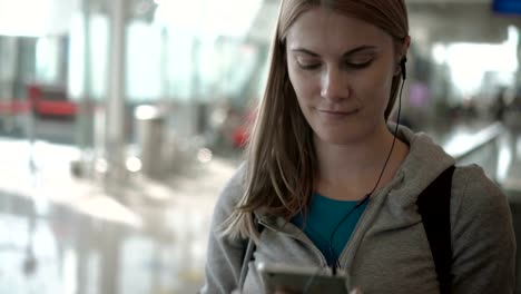 Entspannte-Frau-mit-Travolator-im-Flughafen-terminal.-Verwenden-ihr-Smartphone,-das-Musikhören