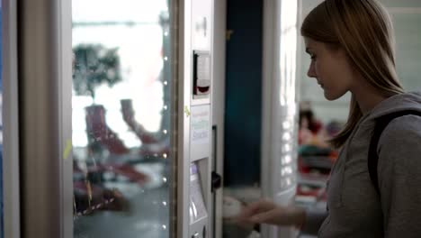 Beautiful-hungry-woman-picking-item-out-of-vending-machine-in-airport-terminal.-Waiting-for-flight