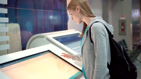 Beautiful-attractive-woman-in-airport-terminal.-Using-touchscreen,-searching-for-flight-information