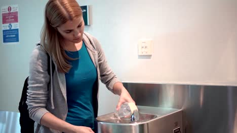 Schöne-Frau-im-Flughafen-terminal.-Stand-in-der-Nähe-Trinkbrunnen-Zeichnung-Wasser-in-Kunststoff-Flasche