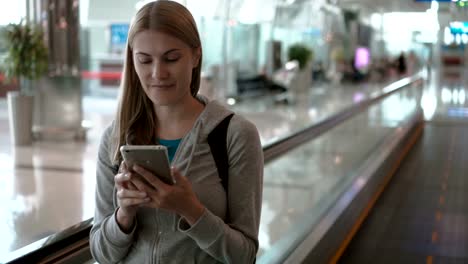 Woman-using-travolator-in-airport-terminal.-Waiting-for-flight.-Using-her-smartphone,-browsing