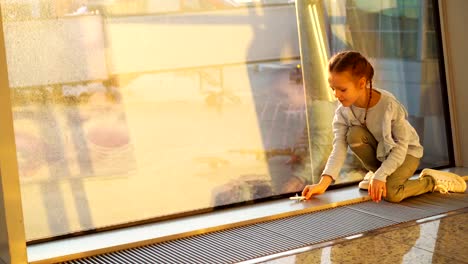 Adorable-niñita-jugando-con-el-pequeño-modelo-de-juguete-de-avión-en-el-aeropuerto-junto-a-la-ventana-grande.-Concepto-de-vuelo-y-avión.