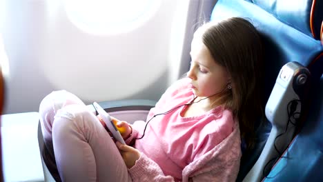 Adorable-niña-viaja-en-un-avión.-Lindo-niño-con-ordenador-portátil-junto-a-la-ventana-en-el-avión