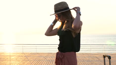 Young-business-lady-with-suitcase-putting-hat-on-at-seafront