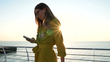 Young-business-lady-with-suitcase-using-smartphone-at-the-seafront