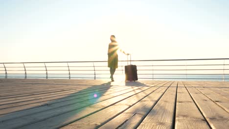 Young-business-lady-with-suitcase-at-the-seafront-during-sunset,-dolly