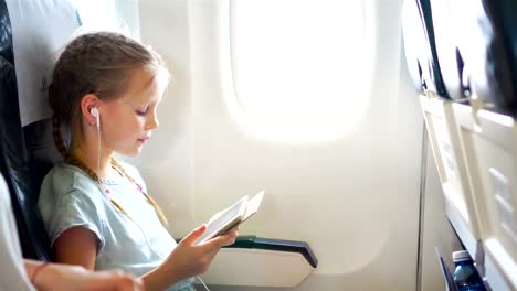 Entzückende-kleine-Mädchen-mit-dem-Flugzeug-reisen.-Süßes-Kind-mit-Laptop-in-der-Nähe-von-Fenster-im-Flugzeug