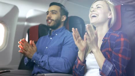 En-la-Junta-de-aterrizaje-acertado-del-avión-comercial-hermosa-joven-Rubio-y-guapo-hispano-hombre-aplaudiendo-piloto.-Interior-de-Aerplane-es-Visible,-el-sol-brilla-a-través-de-la-ventana.