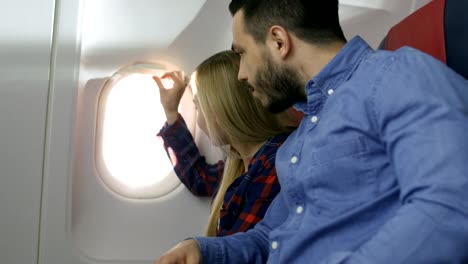 Auf-einem-kommerziellen-Flug-schöne-Blonde-Passagier-öffnet-Fenster-Schatten-und-weckt-schlafende-hispanische-männlichen-Nachbarin.-Neues-Flugzeug-hat-wunderschön-gestalteten-Innenraum.