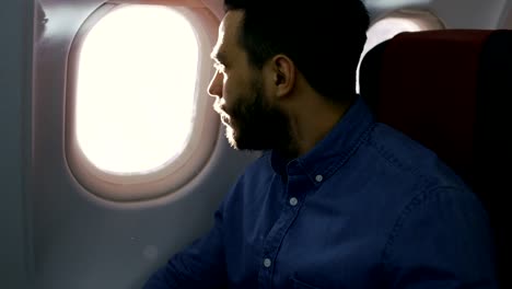 On-a-Transatlantic-Flight-Young-Hispanic-Male-Opens-Shade-and-Looks-out-of-the-Window.