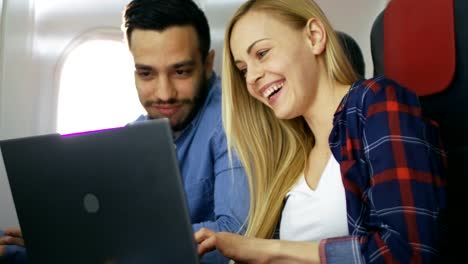 Brautpaar-auf-Transatlantik-Flug-Filme-auf-ihrem-Laptop.-Schöne-Blonde-Mädchen-und-ihr-spanischer-Freund-sind-glücklich-zusammen.