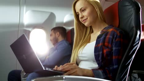 On-Board-of-Commercial-Airplane-Beautiful-Young-Blonde-Works-on-a-Laptop-while-Her-Hispanic-Male-Neighbor-Looks-out-of-the-Window.