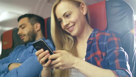 An-Board-des-kommerziellen-Flugzeug-schöne-junge-Blonde-verwendet-Smartphone-während-ihrer-Hispanic-männlichen-Nachbar-schläft.