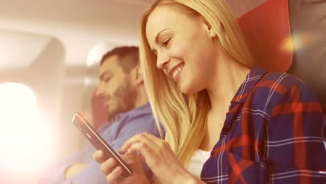 On-Board-of-Commercial-Airplane-Beautiful-Young-Blonde-Uses-Smartphone-while-Her-Hispanic-Male-Neighbor-Sleeps.-Sun-Shines-Through-Plane-Window.