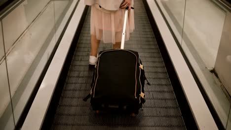 Close-up-view-of-young-woman-with-suitcase-standing-on-the-escalator-in-airport.-Hipster-female-ready-to-going-to-trip
