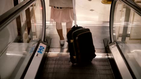 Vista-de-primer-plano-del-joven-elegante-con-pie-de-maleta-en-las-escaleras-mecánicas.-Pies-de-mujer-atractiva-en-el-aeropuerto