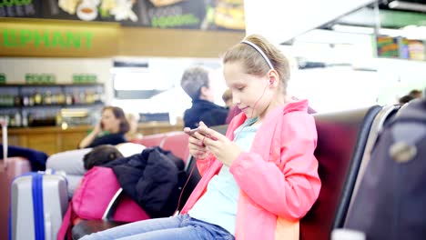 Kleine-Mädchen-spielen-auf-Smartphone-in-Flughafenhalle