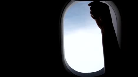 4-K.-jóvenes-viajando-en-avión.-diapositiva-de-mano-chica-hasta-ventana-de-avión-abierta-durante-viajes-en-avión.-cielo-nublado-afuera-de-la-ventana-del-avión.-de-viaje-por-concepto-de-avión