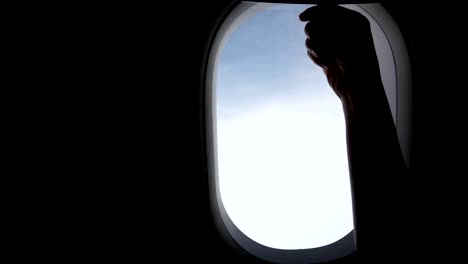 4K.-young-women-traveling-by-plane.-girl-hand-slide-up-to-open-airplane-window-during-air-travel.-cloudy-sky-outside-airplane-window.-travelling-by-airplane-concept