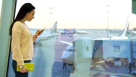 Retrato-de-mujer-joven-con-el-smartphone-en-el-aeropuerto-internacional.-Pasajeros-de-la-aerolínea-en-un-salón-del-aeropuerto-esperando-el-avión-de-vuelo