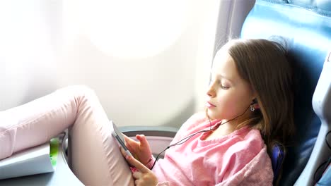 Entzückende-kleine-Mädchen-mit-dem-Flugzeug-reisen.-Süßes-Kind-mit-Laptop-in-der-Nähe-von-Fenster-im-Flugzeug