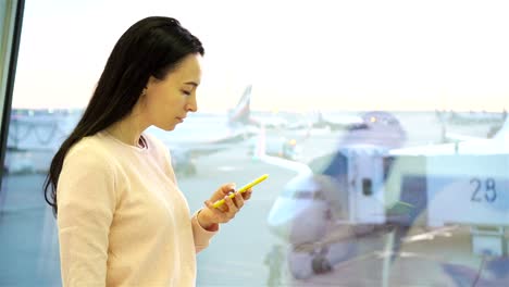 Retrato-de-mujer-joven-con-el-smartphone-en-el-aeropuerto-internacional.-Pasajeros-de-la-aerolínea-en-un-salón-del-aeropuerto-esperando-el-avión-de-vuelo