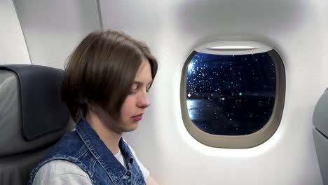 Young-woman-looking-through-window-in-airplane