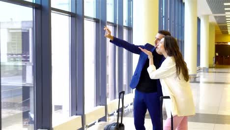 Couple-with-baggage-in-international-airport.-Man-and-woman-taking-selfie-near-big-window-in-aeroport