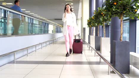 Mujer-joven-con-el-equipaje-en-el-aeropuerto-internacional-de-caminar-con-su-equipaje.-Pasajeros-de-la-aerolínea-en-un-salón-del-aeropuerto-esperando-el-avión-de-vuelo.