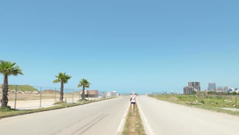 Girl-walks-on-road-near-coastline-and-barbed-fence-of-airport-in-Batumi,-Georgia