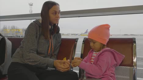 Mother-and-daughter-at-airport.-Little-girl-cleans-mandarin-at-waiting-hall.