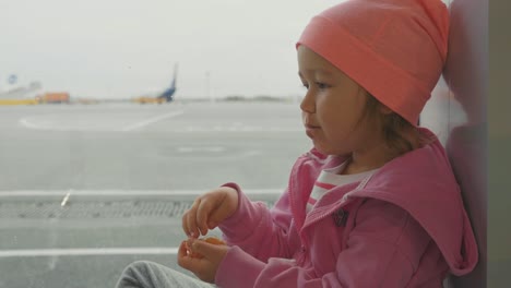 Babymädchen-isst-wenig-ernst-Mandarine-Fensterplatz-am-Flughafen.