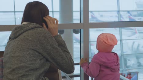 Junge-Mutter-und-Töchterchen-blickt-aus-Fenster-am-Flughafen