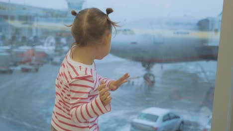 Little-child-girl-looks-out-of-window-on-airplane-and-dancing,-rear-wiew.