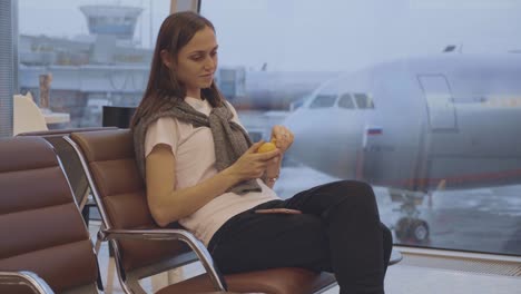 Young-woman-eats-tangerine-at-airport-with-airplane-on-the-background