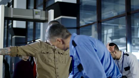 Airport-worker-checking-passenger-with-metal-detector