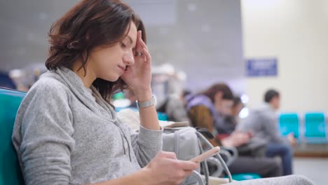 eine-hübsche-Frau-lehnt-sich-auf-ihre-Hand-und-soziale-Netzwerke-auf-einem-Smartphone-sucht,-sie-ist-am-Flughafen