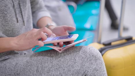 Close-up-shot-of-a-woman's-hands-holding-smartphone-and-passport-in-a-terminal