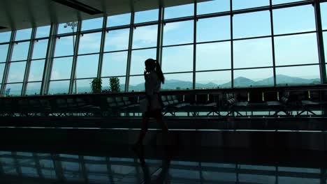 Silhouette-eines-Piloten-zu-Fuß-in-einer-geschäftigen-Flughafen-terminal