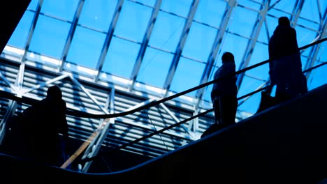 People-silhouettes-on-escalator-moving-in-shopping-center-with-large-windows