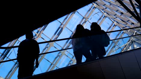 La-ecsalator-de-aeropuerto-de-ventana-de-vidrio-con-silueta-de-personas-en-movimiento