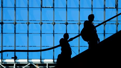 Menschen-Silhouetten-auf-Rolltreppe-innerhalb-der-Shopping-Mall-mit-großen-Fenstern