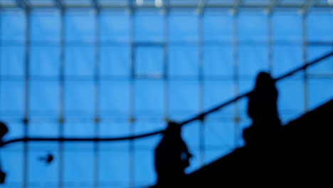 Blur-people-silhouettes-on-escalator-moving-inside-of-airport-with-large-windows